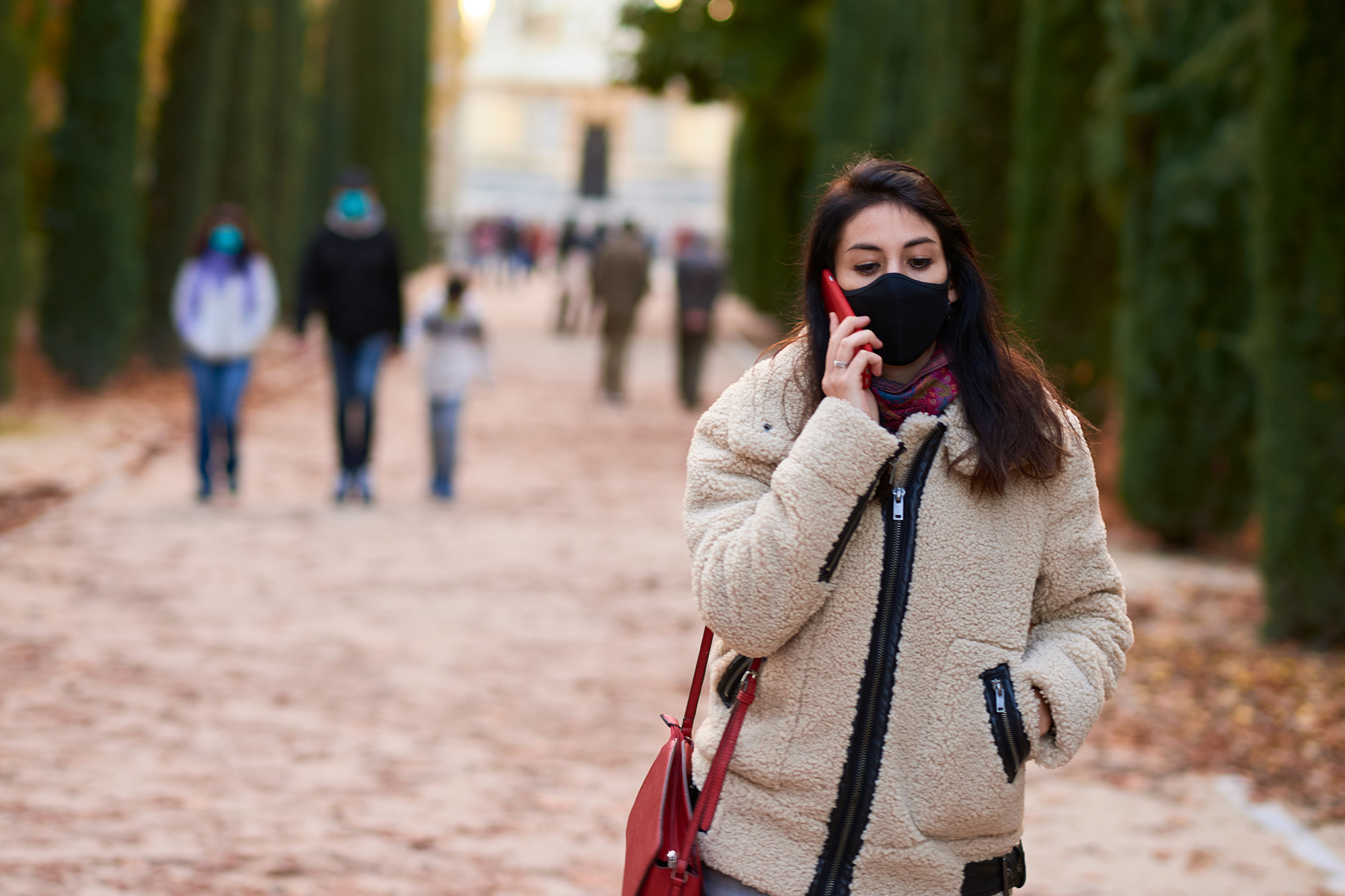 Beautiful woman with mask calling with her smartphone in a park in the coronavirus autumn
