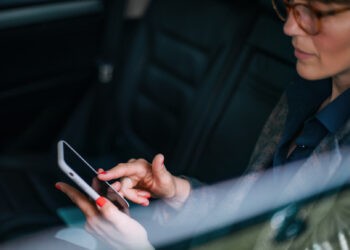 Красивая деловая женщина средних лет сидит в машине, пользуется мобильным телефоном и пишет текстовые сообщения