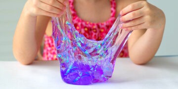 Hand holding homemade toy called Slime, kids having fun and being creative by science experiment. Close up of a little girl is hand playing a purple slime