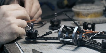 Guy soldering drone FPV wires. Front frame view. Workshop