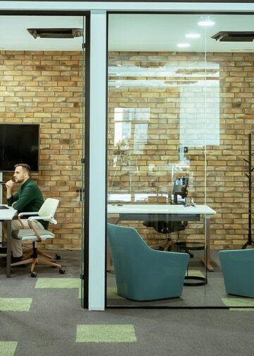Dwóch profesjonalistów prowadzi rozmowę, siedząc wygodnie w salonie biurowym, otoczonym zielenią i nowoczesnymi elementami wystroju